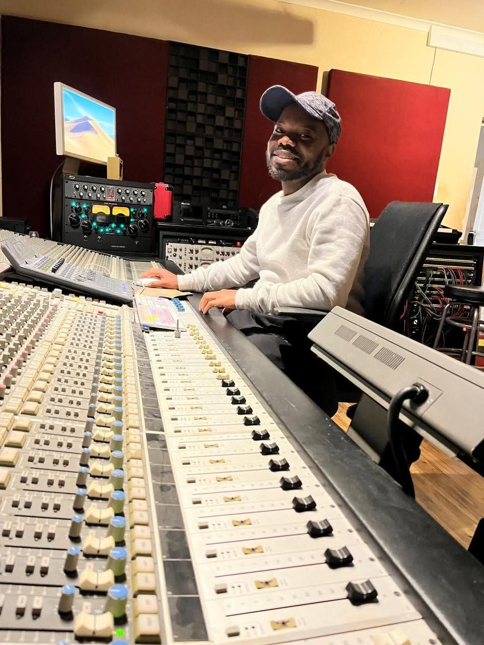 Smiling producer seated at a large analogue mixing console with outboard processing behind