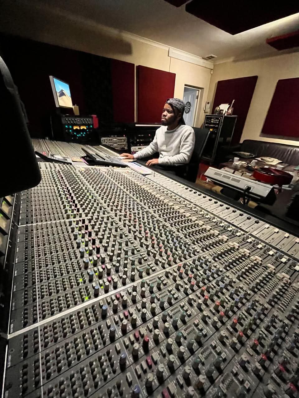 Wide view across a large mixing console with the engineer at work and acoustic panels behind