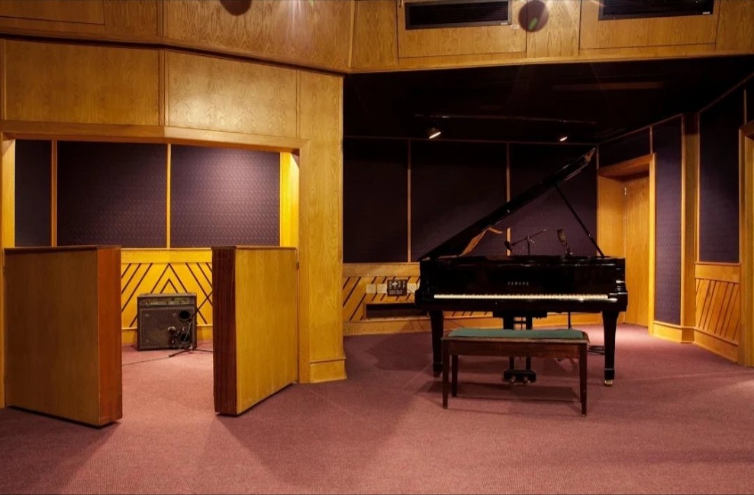 Grand piano with bench in a wood-panelled live recording room